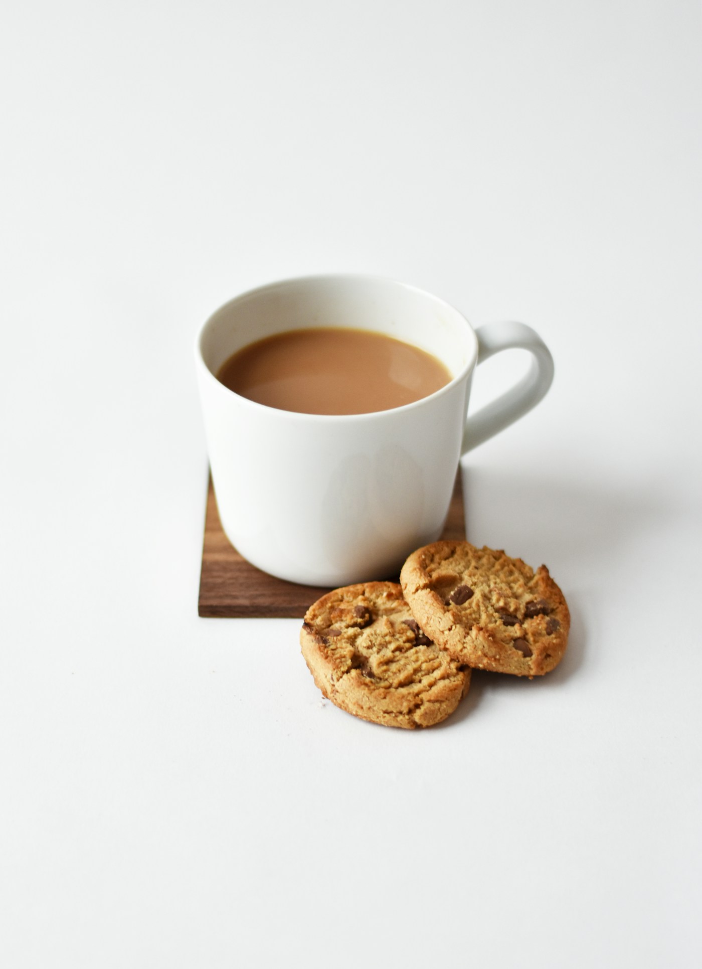 A warm drink in a white cup beside cookies